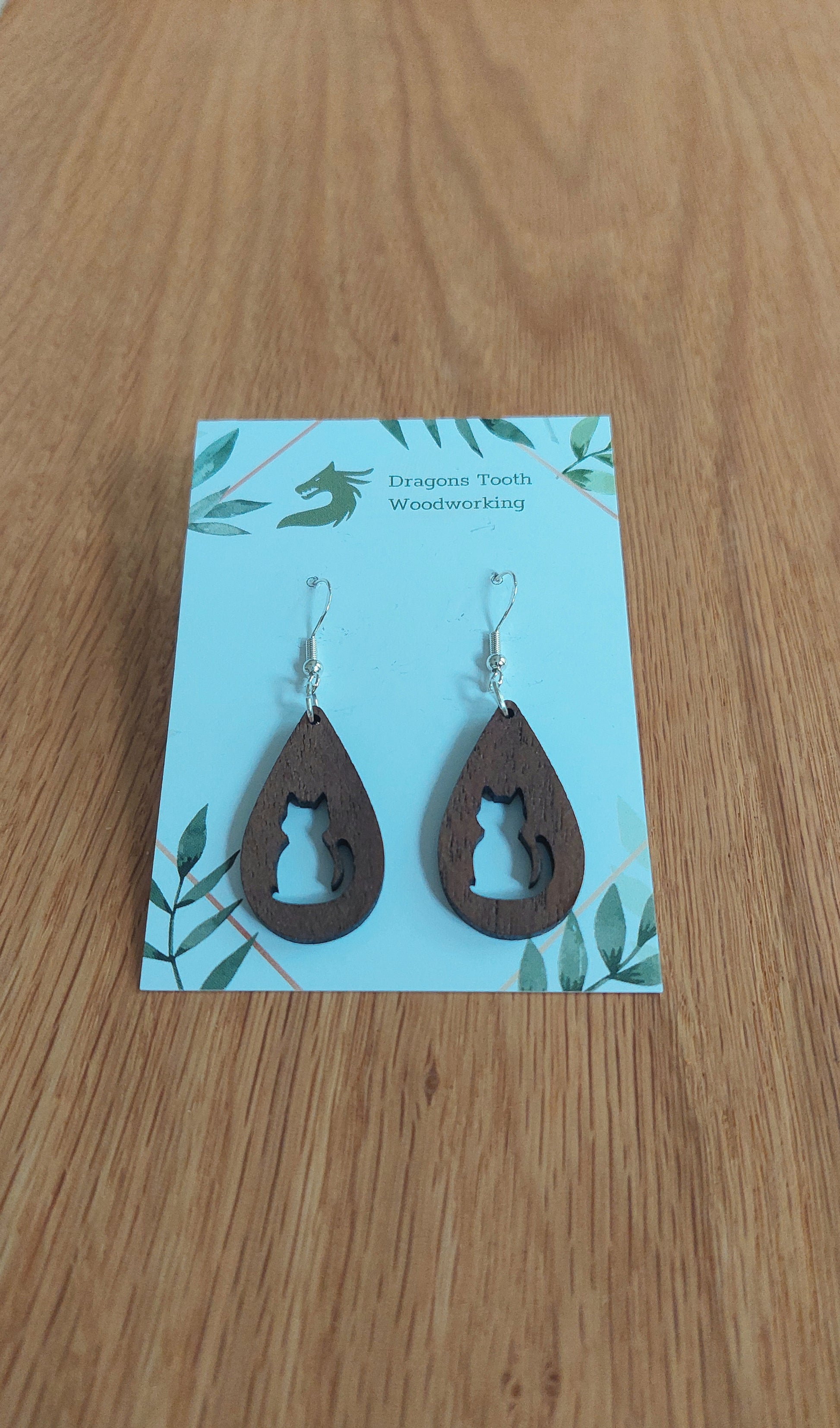 A front view of the circular cat silhouette earrings crafted from rich, deep chocolate-brown solid Walnut wood, displayed on an earring card.