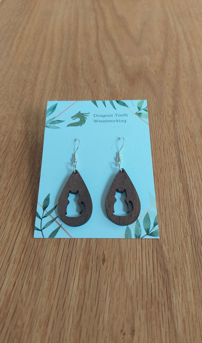 A front view of the circular cat silhouette earrings crafted from rich, deep chocolate-brown solid Walnut wood, displayed on an earring card.