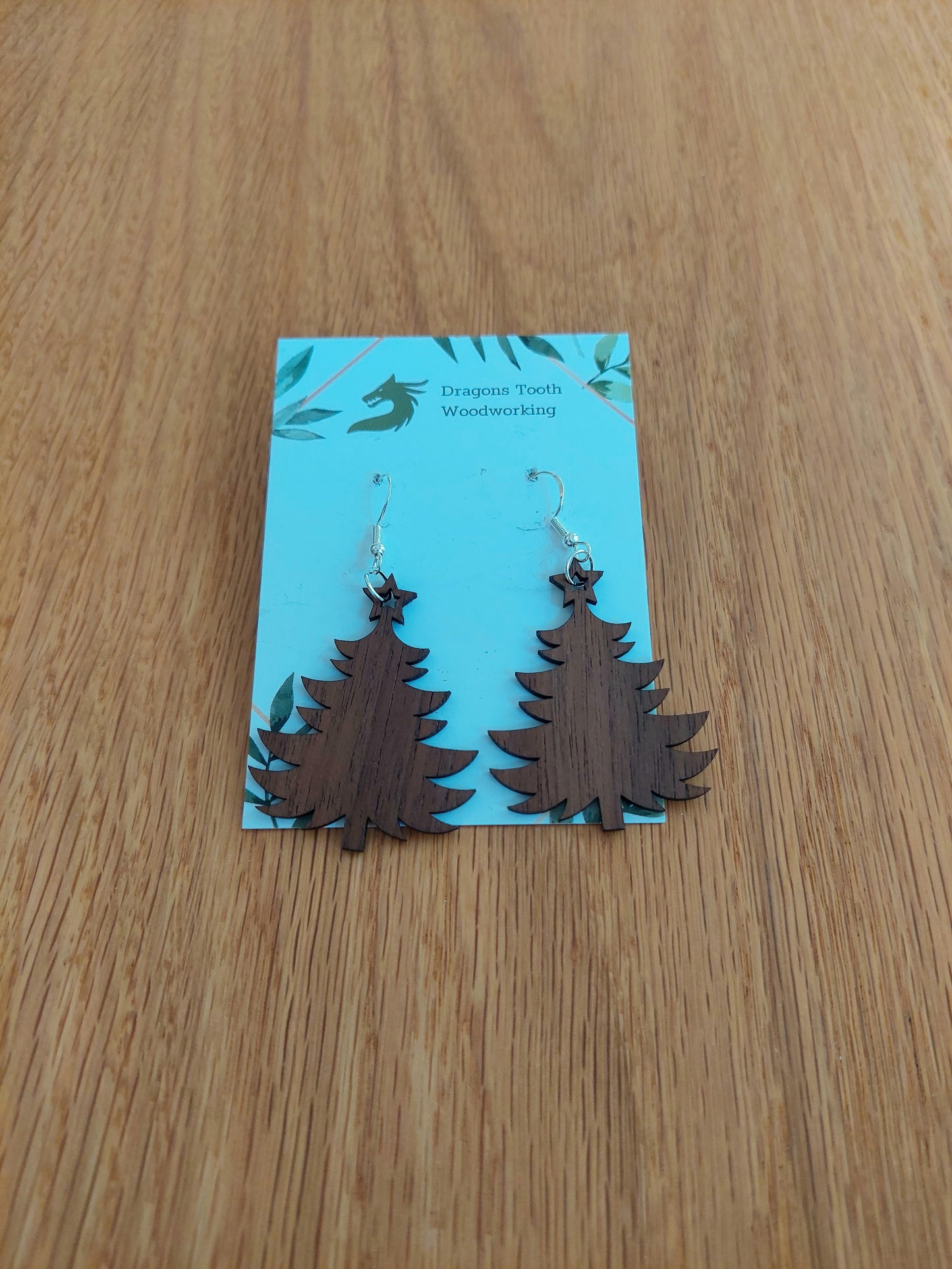 A front view of the Christmas tree earrings crafted from rich, deep chocolate-brown solid Walnut wood, displayed on an earring card.