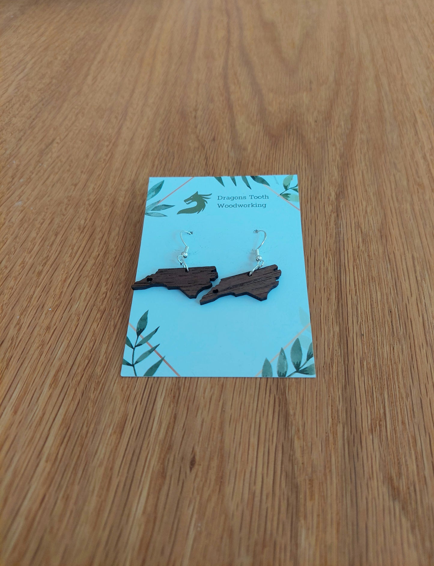 Walnut earrings cut in the shape of the state of north carolina with a heart cutout located where Asheville is
