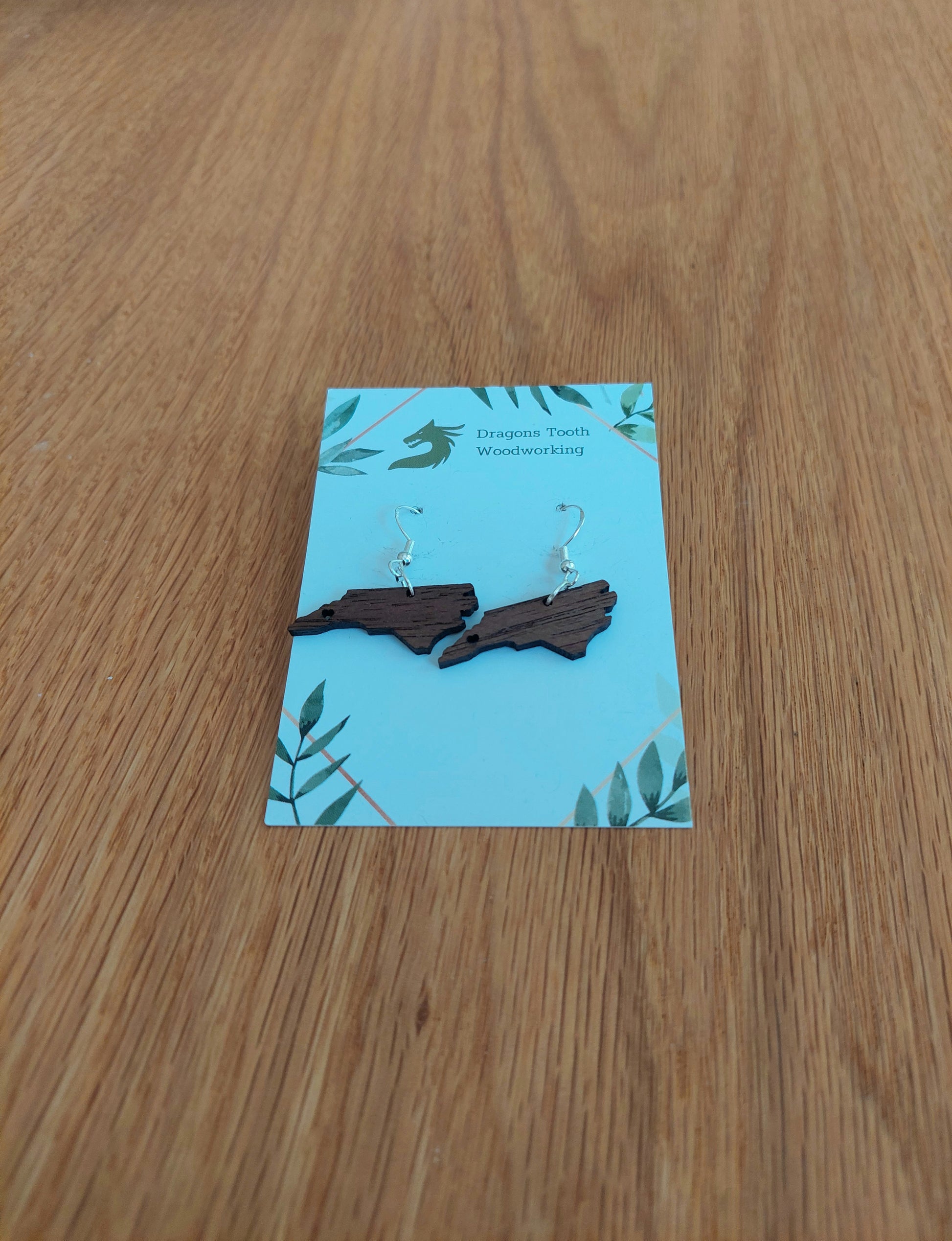 Walnut earrings cut in the shape of the state of north carolina with a heart cutout located where Asheville is