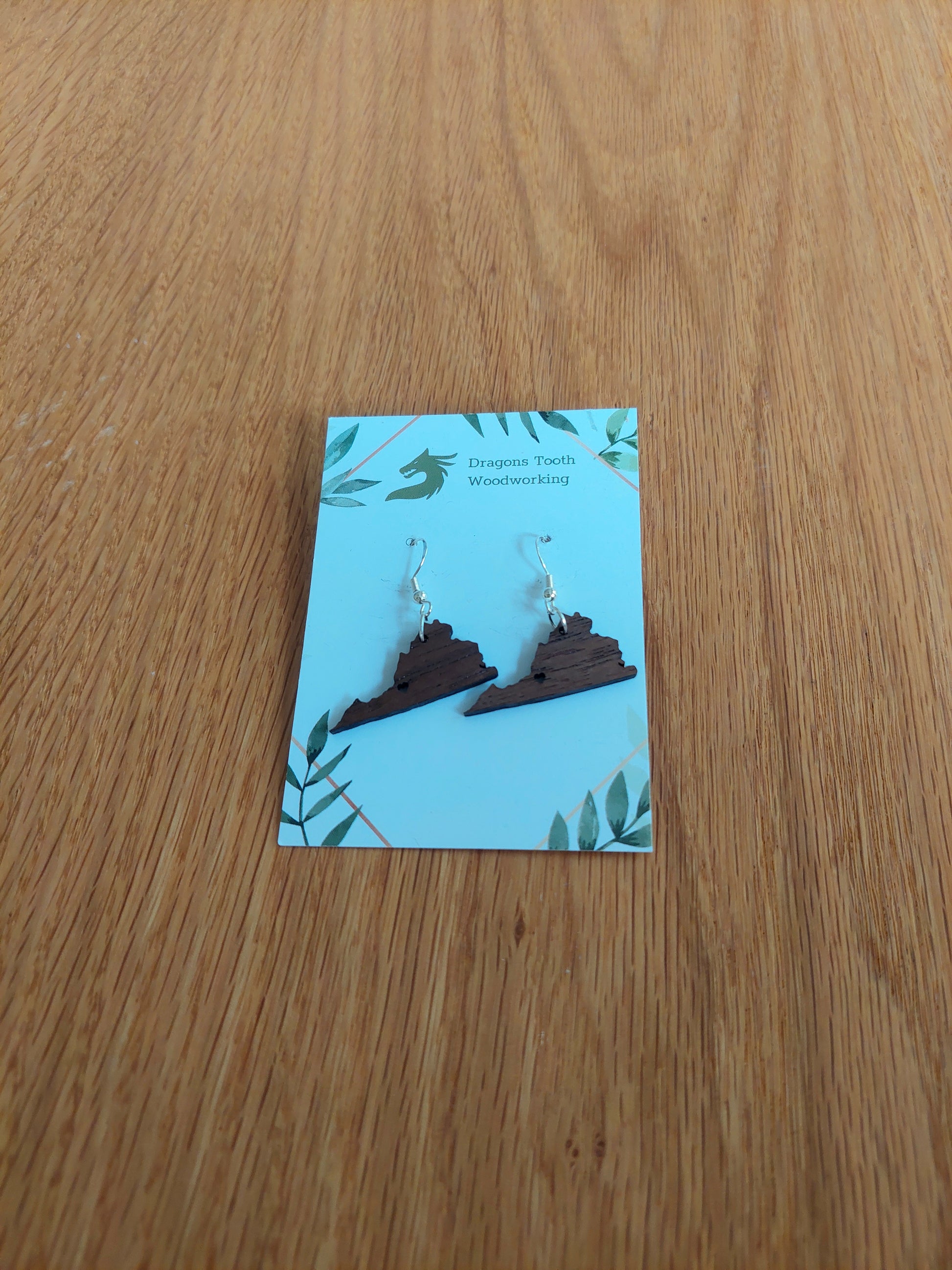 A front view of natural walnut earrings featuring a silhouette of the state of Virginia with a star cutout located where the city of Roanoke is.