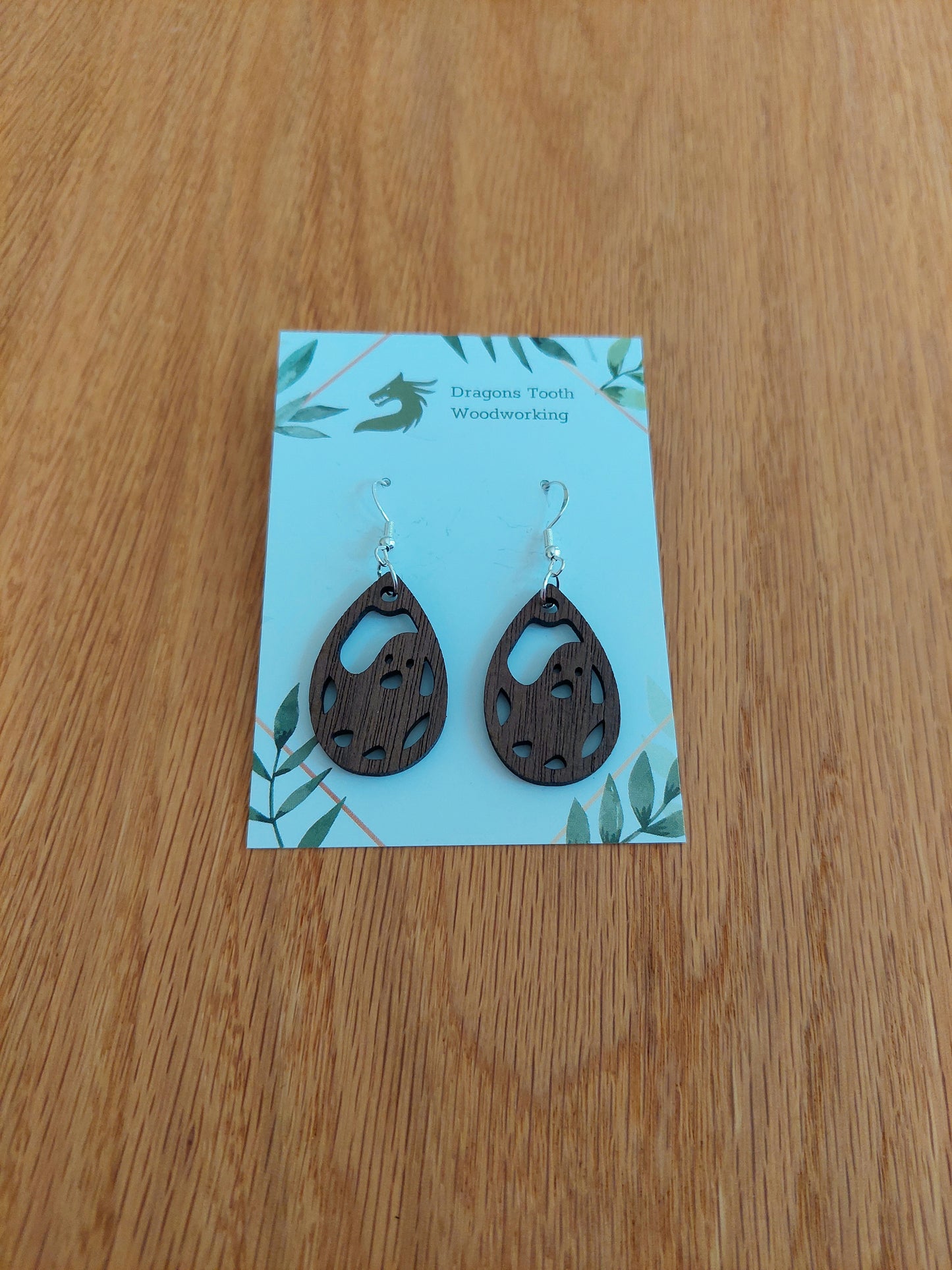 A front view of the friendly ghost earrings crafted from rich, deep chocolate-brown solid Walnut wood, displayed on an earring card.