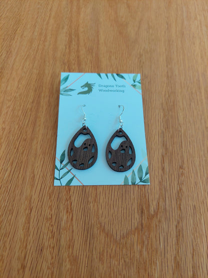 A front view of the friendly ghost earrings crafted from rich, deep chocolate-brown solid Walnut wood, displayed on an earring card.