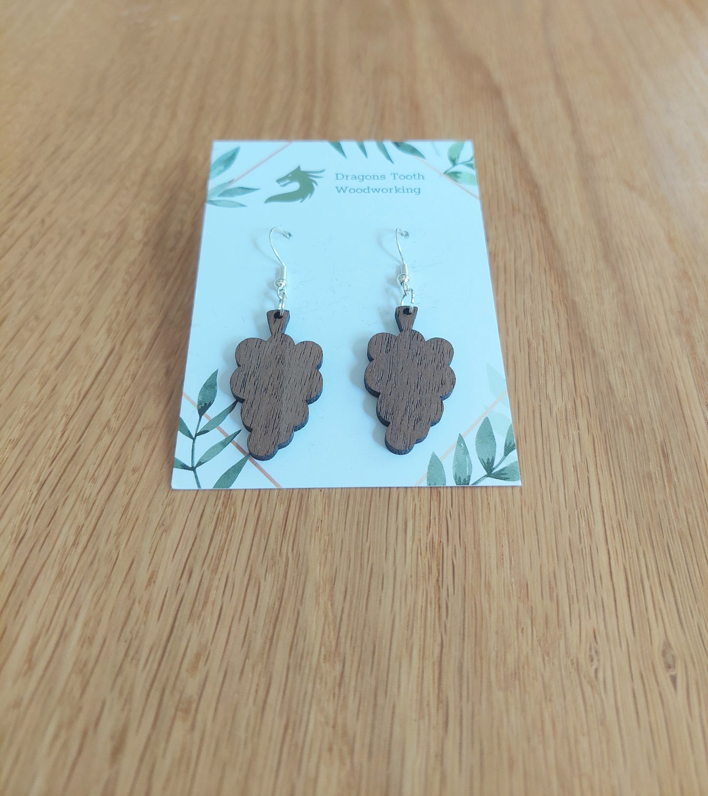 A front view of the grape cluster earrings crafted from rich, deep chocolate-brown solid Walnut wood, displayed on an earring card.