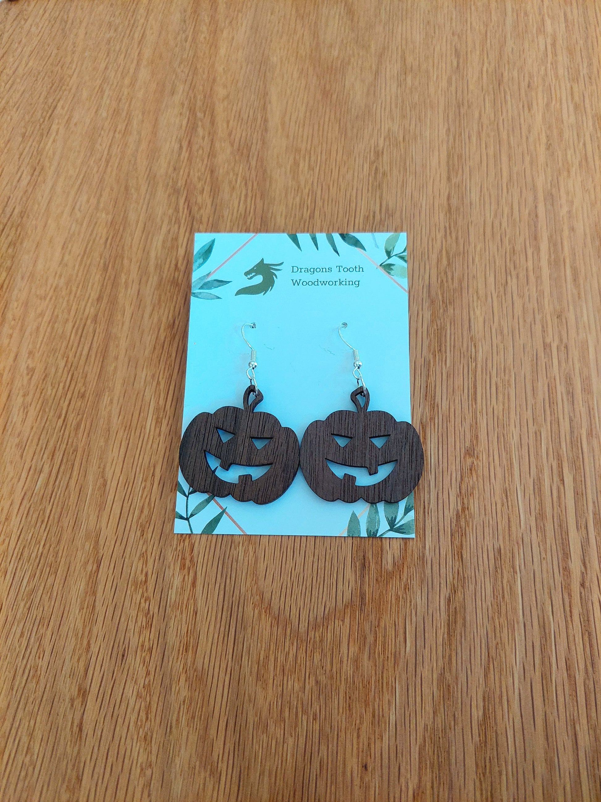 A front view of the festive jack-o'-lantern earrings crafted from rich, deep chocolate-brown solid Walnut wood, displayed on an earring card.