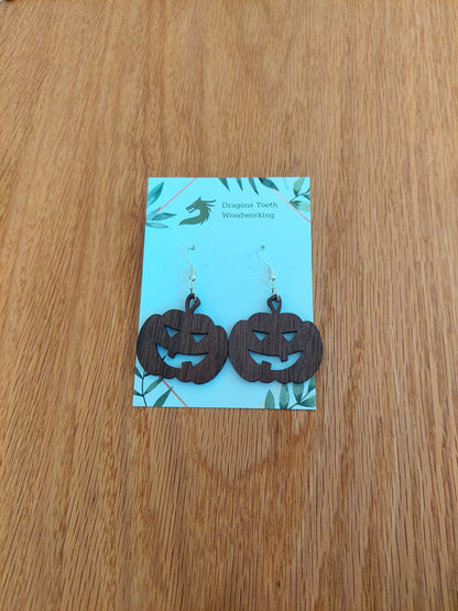 A front view of the festive jack-o'-lantern earrings crafted from rich, deep chocolate-brown solid Walnut wood, displayed on an earring card.