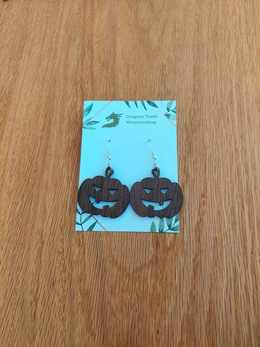 A front view of the festive jack-o'-lantern earrings crafted from rich, deep chocolate-brown solid Walnut wood, displayed on an earring card.