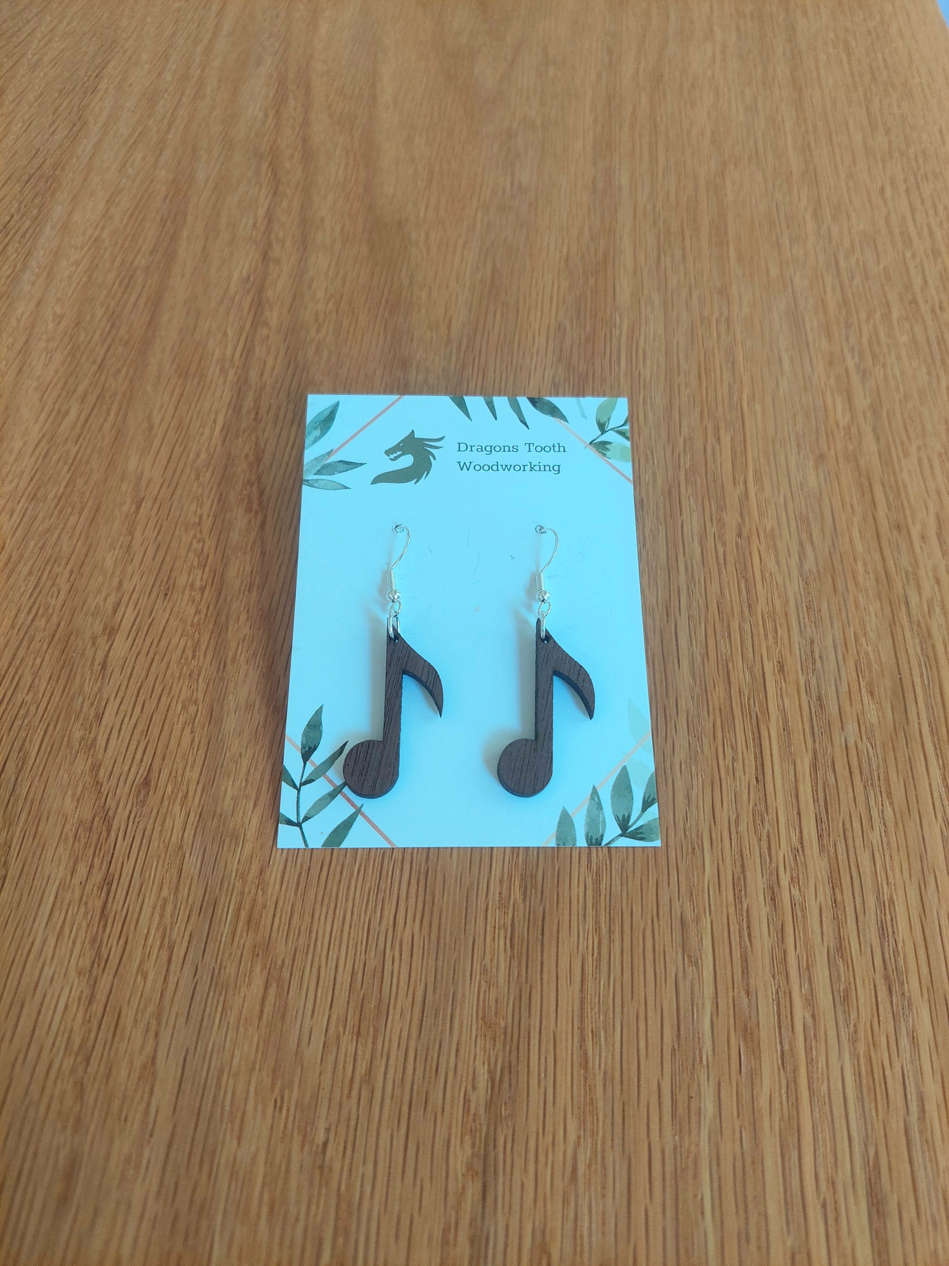 A front view of the circular music note earrings crafted from rich, deep chocolate-brown solid Walnut wood, displayed on an earring card.