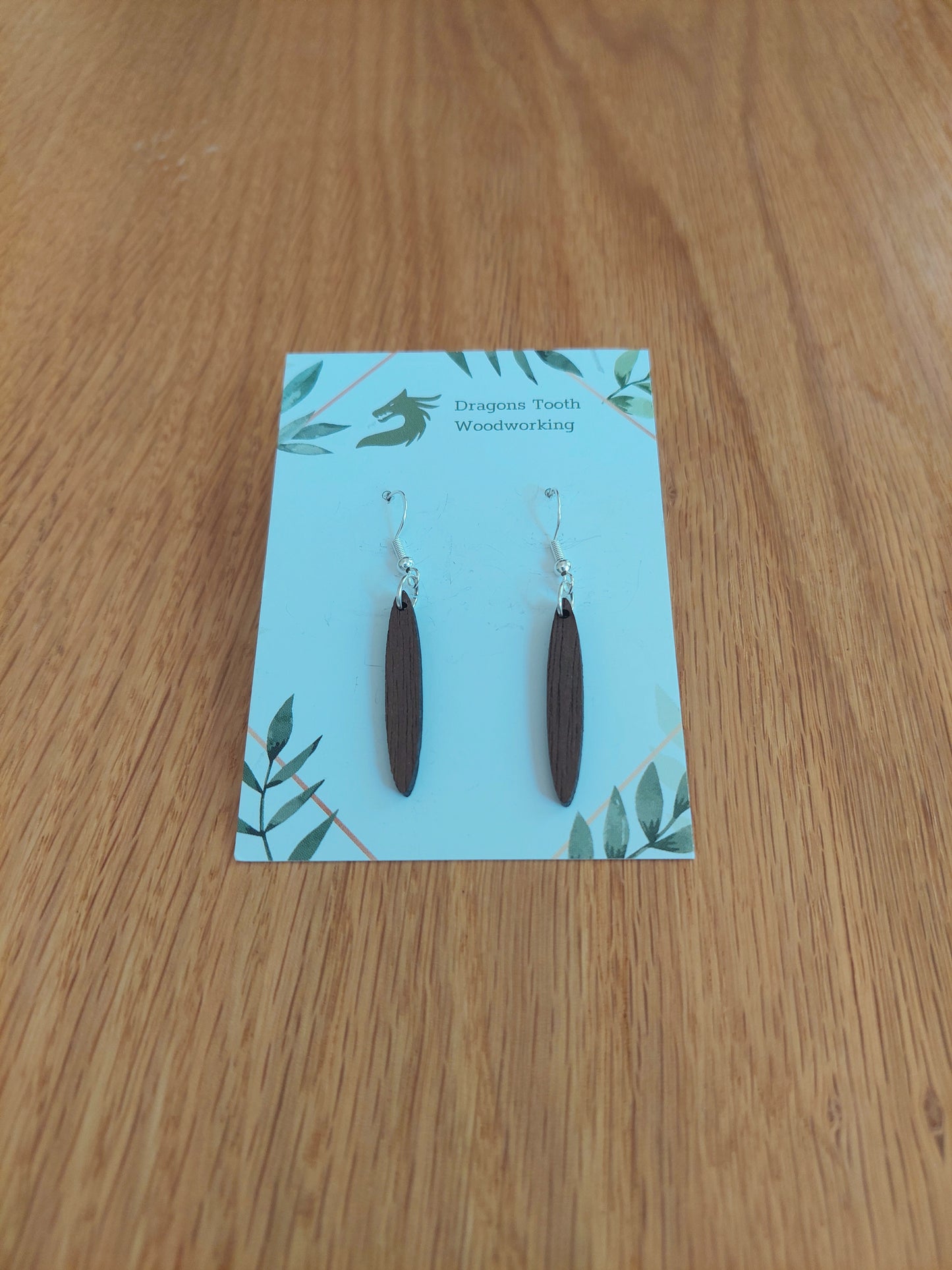A front view of the minimalist open oval earrings crafted from rich, deep chocolate-brown solid Walnut wood, displayed on an earring card.