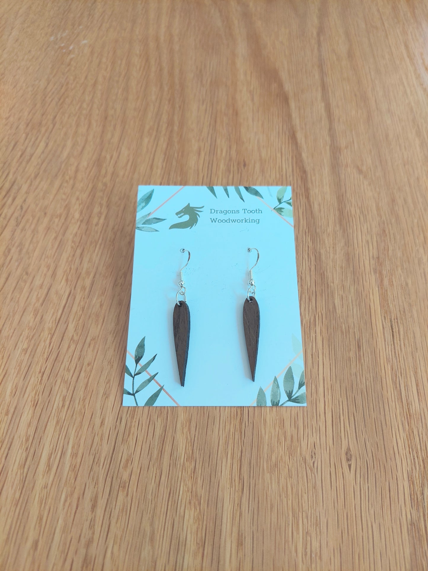 A front view of the minimalist pointed geometric earrings crafted from rich, deep chocolate-brown solid Walnut wood, displayed on an earring card.