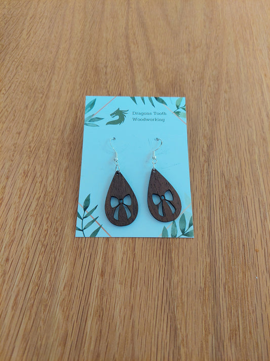 A front view of the ribbon bow teardrop earrings crafted from rich, deep chocolate-brown solid Walnut wood, displayed on an earring card.