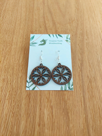 A front view of the classic snowflake silhouette earrings crafted from rich, deep chocolate-brown solid Walnut wood, displayed on an earring card.