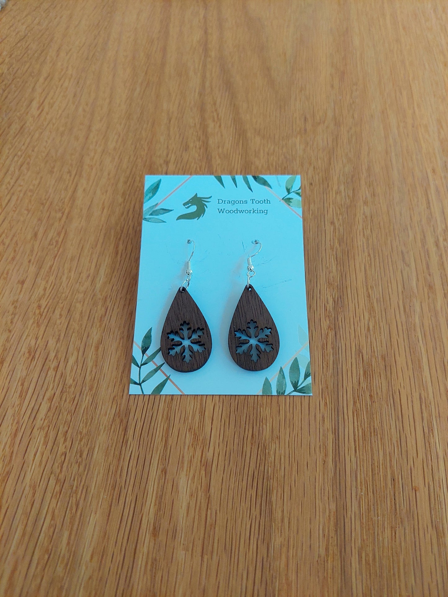 A front view of the snowflake teardrop earrings crafted from rich, deep chocolate-brown solid Walnut wood, displayed on an earring card.