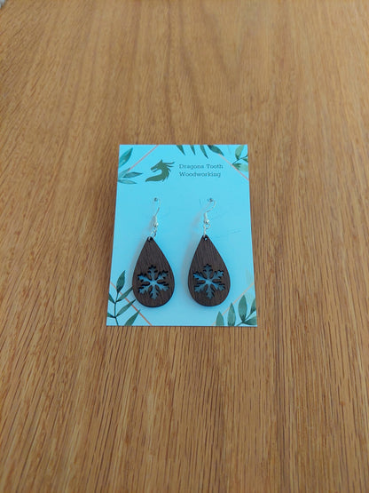 A front view of the snowflake teardrop earrings crafted from rich, deep chocolate-brown solid Walnut wood, displayed on an earring card.