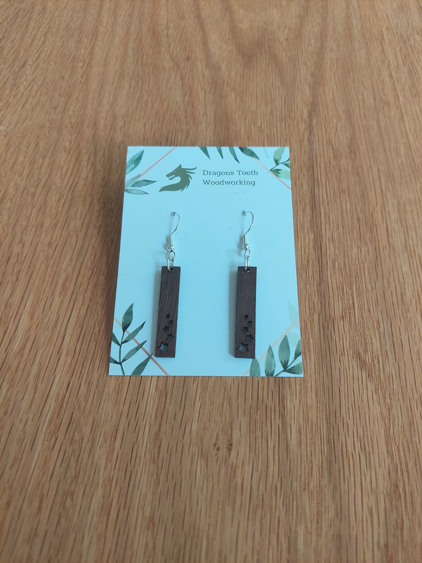 A front view of the minimalist star shower earrings crafted from rich, deep chocolate-brown solid Walnut wood, displayed on an earring card.
