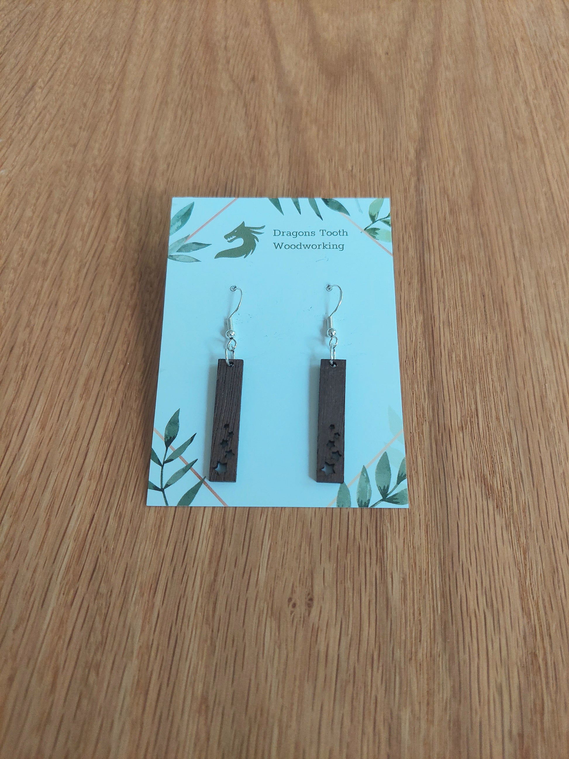 A front view of the minimalist star shower earrings crafted from rich, deep chocolate-brown solid Walnut wood, displayed on an earring card.