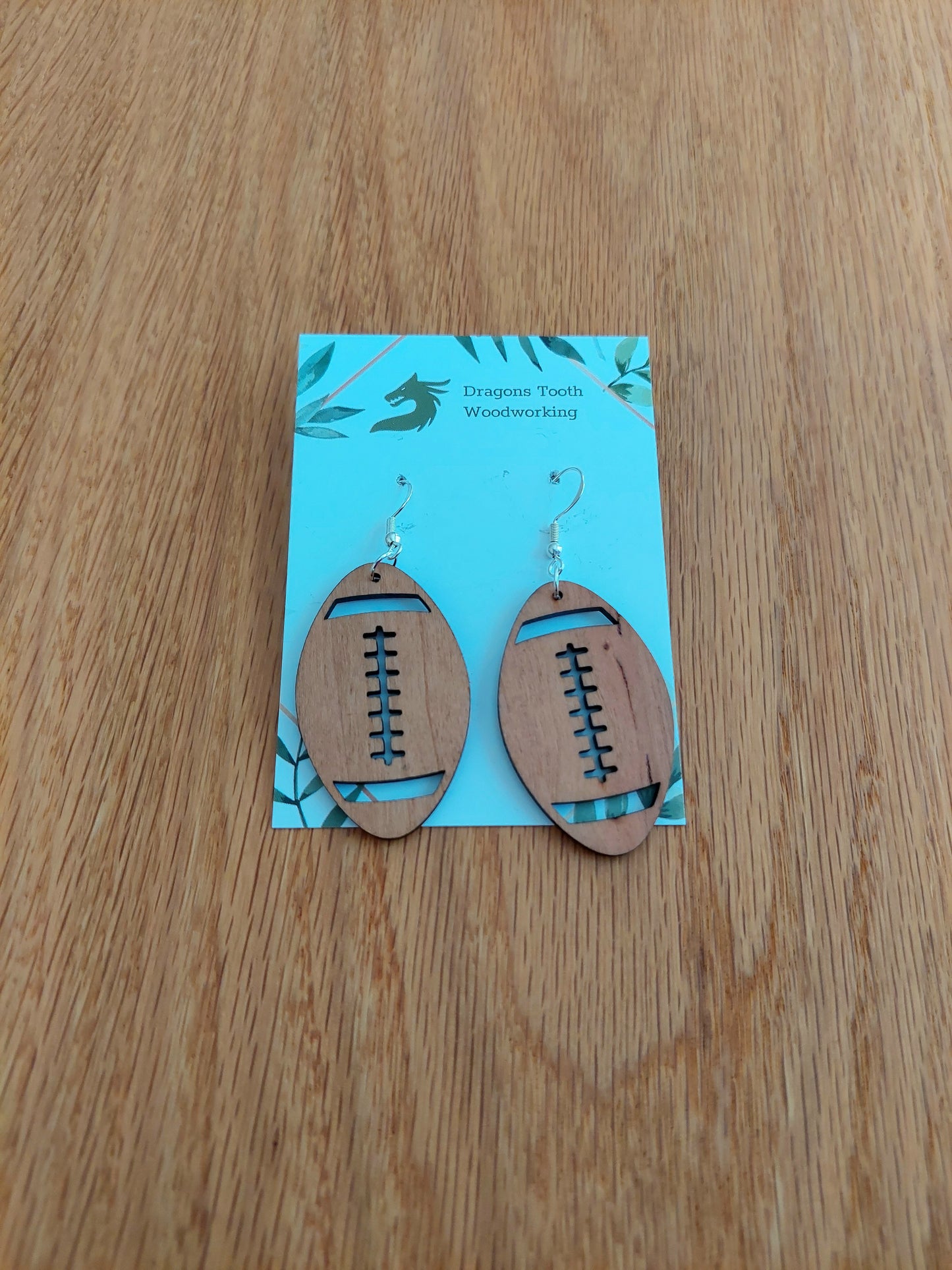 Handcrafted cherry wood football dangle earrings showcasing warm caramel-colored natural wood grain with hypoallergenic hooks.
