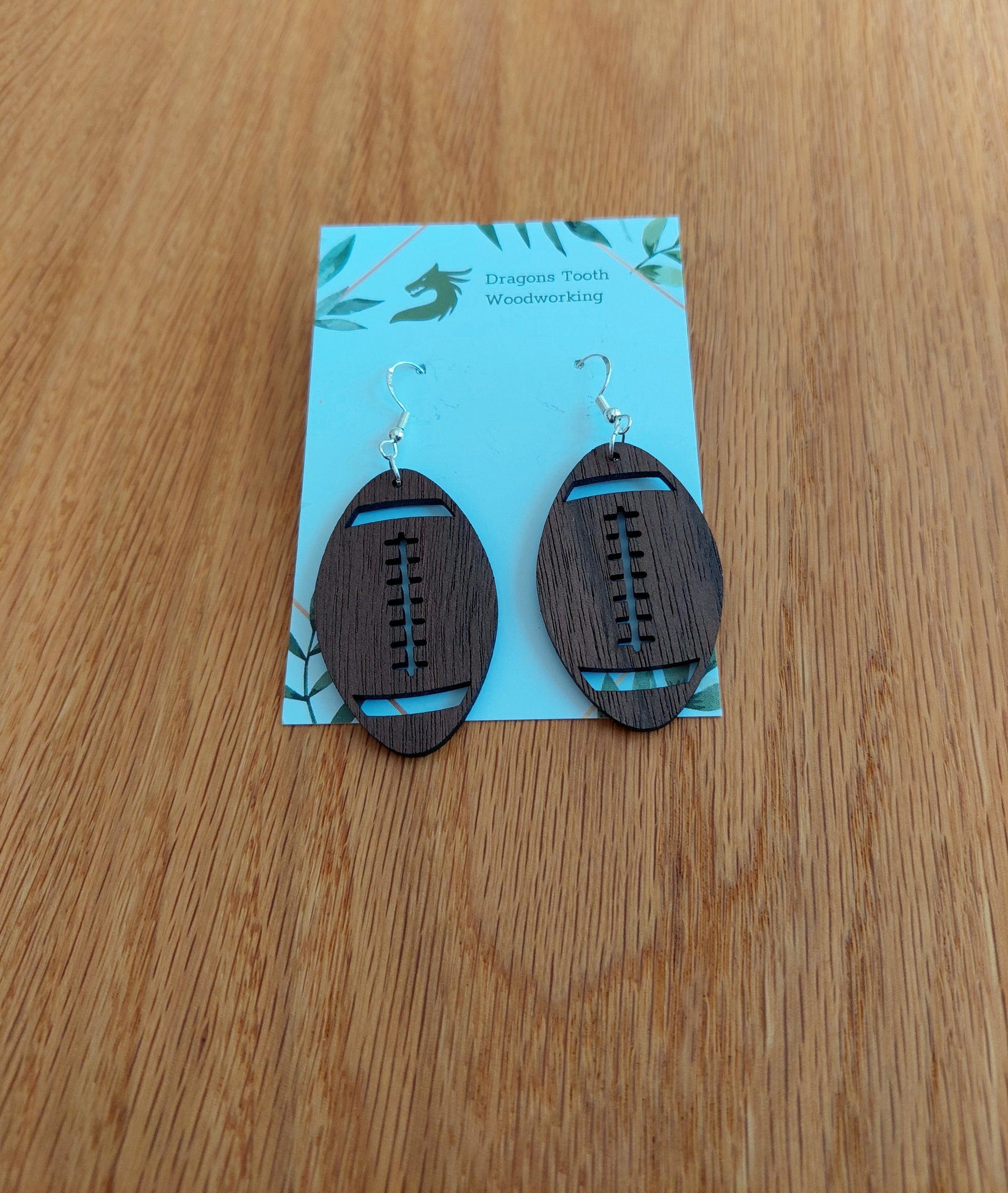 Deep chocolate brown walnut wood football earrings featuring a laser-cut texture and laces, mimicking a real leather football.