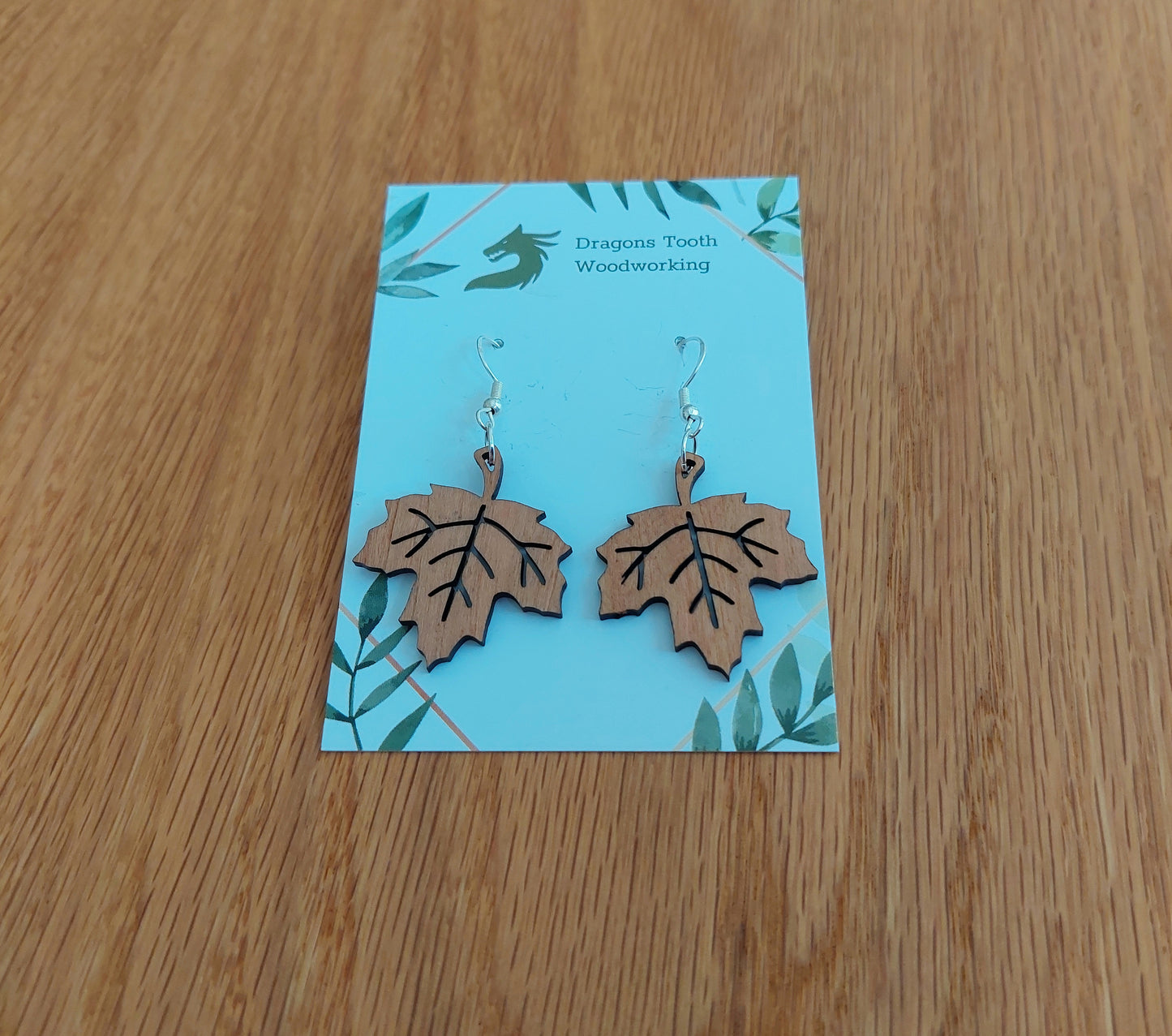 Handcrafted cherry wood maple leaf dangle earrings featuring caramel-toned natural wood grain and sterling silver plated hooks.