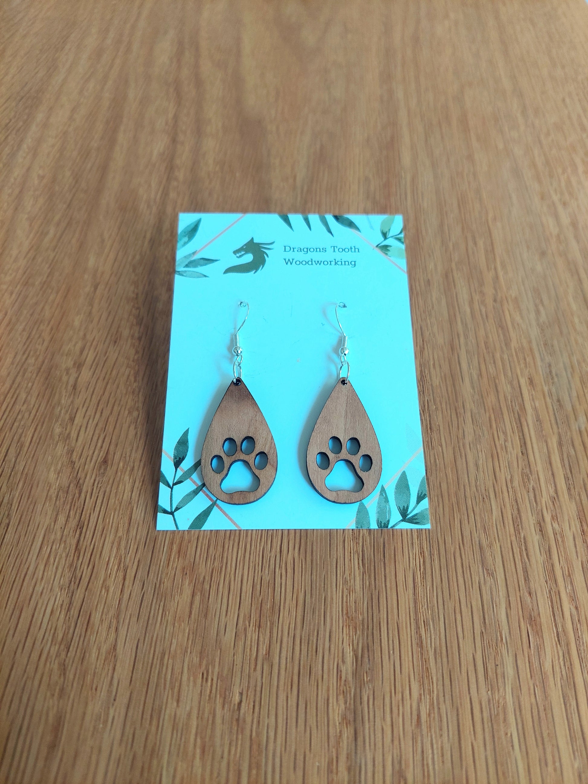 Handcrafted cherry wood pawprint dangle earrings showcasing warm caramel-toned natural wood grain and sterling silver plated hooks.