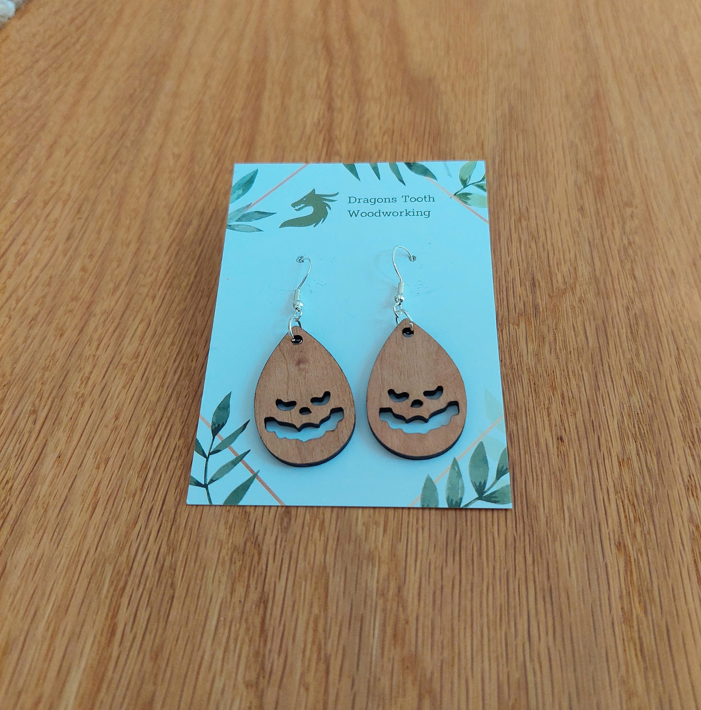Handcrafted cherry wood jack-o-lantern teardrop earrings featuring a warm caramel, pumpkin-toned natural wood grain.